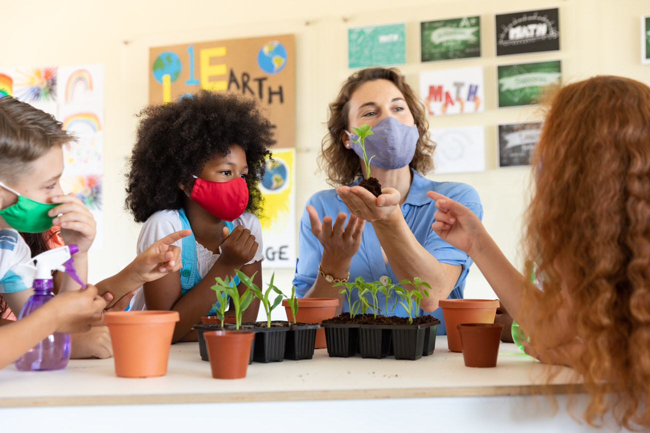 Female teacher wearing face mask showing plant pots to students in class